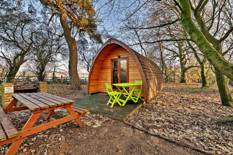 Træ glamping pod med grønne havemøbler og picnicbord i en skov ved Suffolk Woodland Retreat.