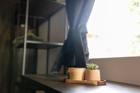 Rebord de fenêtre dans un chalet avec une petite plante et une bougie posées sur un plateau en bois près du rideau.