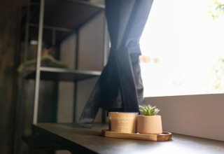 Rebord de fenêtre dans un chalet avec une petite plante et une bougie posées sur un plateau en bois près du rideau.