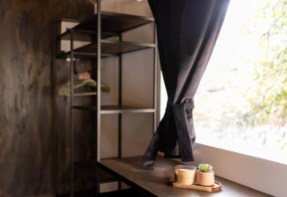 Intérieur de chalet chaleureux avec étagères ouvertes, rideaux noirs et plateau avec tasses et plante.