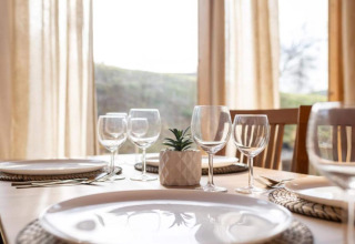 Table dressée dans un chalet, verres à vin, assiettes et une petite plante ornent le centre de la table.