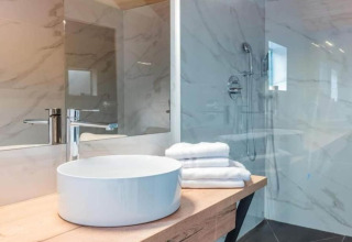Salle de bain moderne de chalet avec vasque ronde, plan en bois, miroir et murs en marbre avec douche.