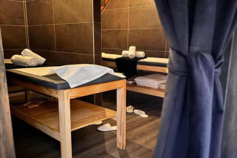 Cabine de spa dans un chalet, deux tables de massage, serviettes roulées et chaussons au sol.