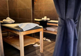 Cabine de spa dans un chalet, deux tables de massage, serviettes roulées et chaussons au sol.