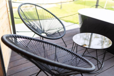 Chaises noires modernes et petite table sur terrasse en bois d’un chalet avec vue sur la pelouse.