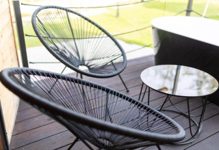 Chaises noires modernes et petite table sur terrasse en bois d’un chalet avec vue sur la pelouse.