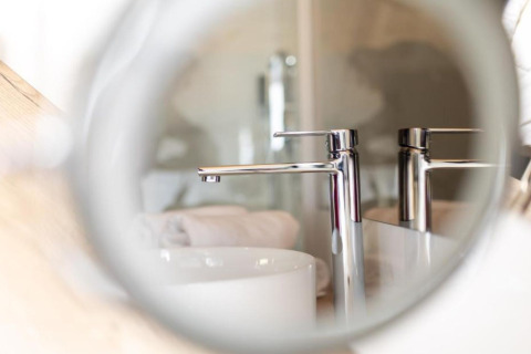 Gros plan d’un robinet moderne aperçu à travers un miroir rond au Halicanum Glamping Peaceful Retreat en Croatie.