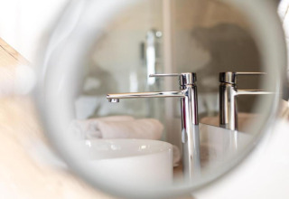 Gros plan d’un robinet moderne aperçu à travers un miroir rond au Halicanum Glamping Peaceful Retreat en Croatie.