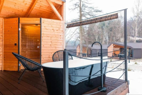 Baignoire extérieure et terrasse en bois au Halicanum Glamping Peaceful Retreat Resort 16 en Croatie, avec cabanes autour.