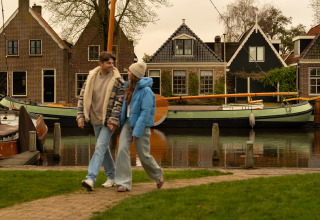 Coppia che cammina mano nella mano al MarinaPark Beach Resort Soal, Friesland, Paesi Bassi, con barche e case dietro.