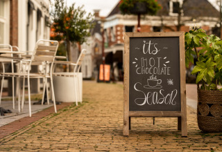 Een stoepbord voor een café in Nederland met 'it's hot chocolate season', omringd door planten.