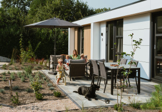 Family relaxing on sunny patio with umbrella, children playing, and black dog at MarinaPark Residentie, Netherlands.