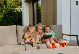 Three young children sit together on an outdoor sofa at MarinaPark Residentie Bloemendaal, looking at a tablet.