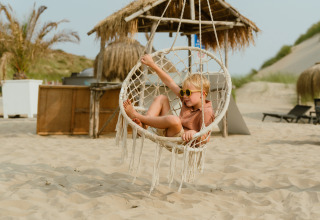 Un enfant avec des lunettes de soleil se détend dans une balançoire sur la plage au MarinaPark Residentie Bloemendaal.