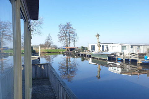 Blick von Hausboot Luxury chalet 55 in den Niederlanden mit ruhigem Wasser und Bäumen sowie Häusern.