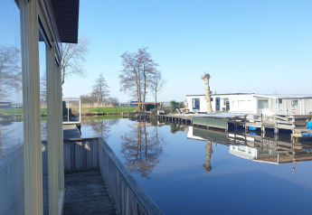 Vue depuis le bateau-maison Luxury chalet 55 aux Pays-Bas, eau calme, arbres et reflets visibles.