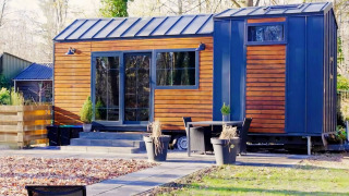 Charming Tiny House con esterno in legno e dettagli blu, immersa nel verde con arredi da giardino.