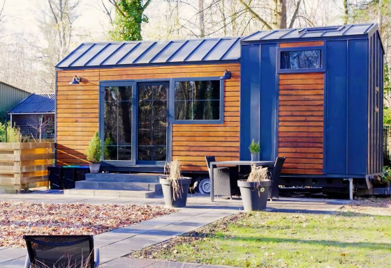 Charming Tiny House met houten gevel en blauwe accenten, gelegen in een tuin met terrasmeubilair.