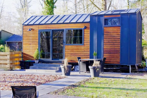 Charming Tiny House de madera y detalles azules, rodeada de naturaleza y muebles de jardín modernos.