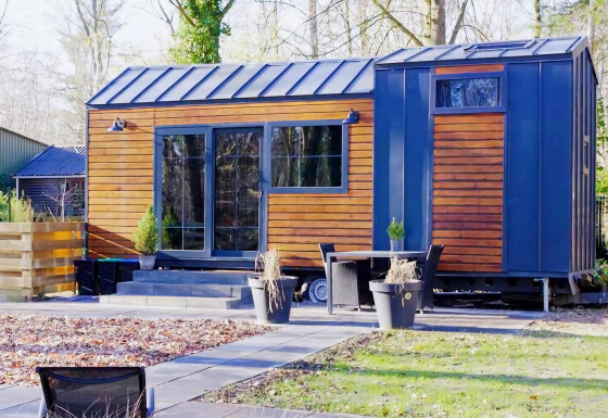 Charming Tiny House de madera y detalles azules, rodeada de naturaleza y muebles de jardín modernos.