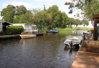 Uitzicht op een kanaal met boten en woonboten bij Luxury chalet 55 in Nederland, omringd door bomen.