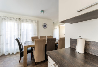 Dining area with six brown chairs, wooden table, modern kitchen countertop in Dutch houseboat.