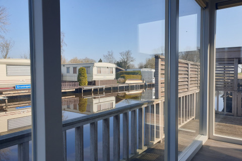 Vista desde la casa flotante Luxury chalet 55 en Países Bajos, con terraza y reflejo del agua tranquila.