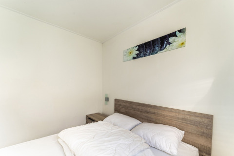 Soveværelse med dobbeltseng, træhovedgærde, natbord og vægkunst på en husbåd i Holland.