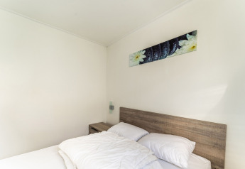 Dormitorio con cama doble, cabecero de madera, mesita y arte en la pared en una casa flotante en Holanda.