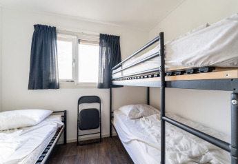 Bright room on a houseboat with bunk beds, white bedding, window with dark curtains, and wood flooring.
