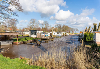 Vista de casas flotantes y chalets de lujo en un canal en los Países Bajos, rodeados de césped y árboles.