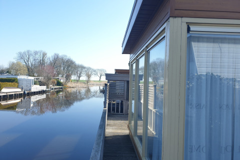 Vue depuis le houseboat Luxury chalet 55 aux Pays-Bas, avec eau calme, arbres et ciel clair réfléchis.