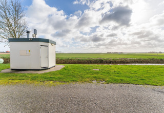 Small white building on a green lawn near a ditch under a partly cloudy sky in the Netherlands.