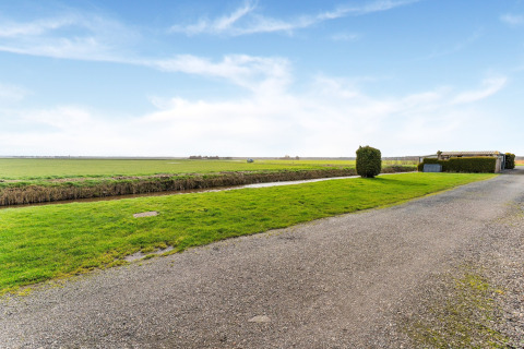 Grindweg, groene weide en kanaal bij huisboot Luxury chalet 55 op het Nederlandse platteland.