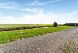 Blick auf einen Kiesweg, grüne Wiesen und einen Kanal beim Hausboot Luxury chalet 55 in den Niederlanden.