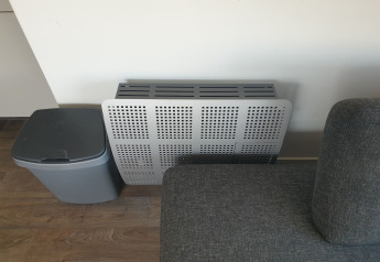 Cubierta de radiador, sofá gris y papelera en el acogedor salón de la casa flotante Luxury chalet 55 en Países Bajos.