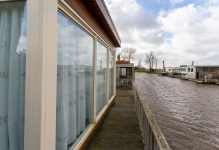 Zicht vanaf een woonboot met grote ramen en houten terras op het water bij Luxury chalet 54 Bantega, Nederland.