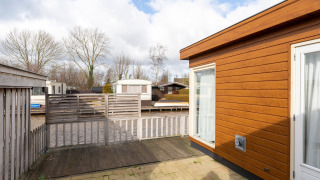 Uitzicht op het terras van Luxury chalet 54 Bantega, met houten gevel en omheining onder een bewolkte lucht.