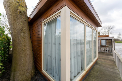 Angolo esterno della houseboat Luxury chalet «54 Bantega» nei Paesi Bassi, con ampie vetrate e un albero.