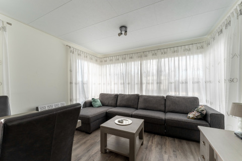 Wohnzimmer mit großem grauen Ecksofa, Couchtisch und hellen Vorhängen im Luxus-Chalet '54 Bantega' in den Niederlanden.