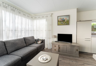 Lichte woonkamer op woonboot ‘Luxury chalet 54 Bantega’ in Nederland met grijze zetel en tv.