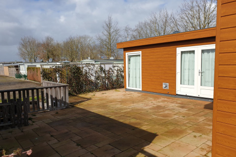 Zonnig terras bij luxe chalet 54 Bantega, met uitzicht op woonboten en bomen in Nederland.
