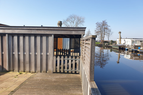 View of a wooden terrace, fence, and houseboat at Luxury chalet 54 Bantega in the Netherlands, by water.
