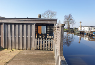View of a wooden terrace, fence, and houseboat at Luxury chalet 54 Bantega in the Netherlands, by water.