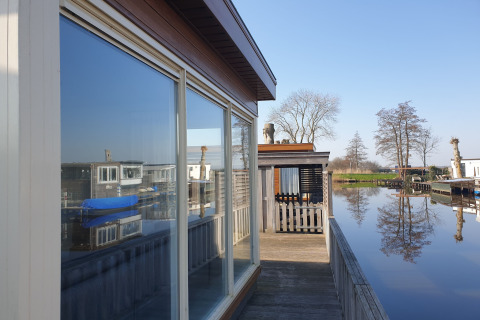 Blick auf das Hausboot Luxury chalet „54 Bantega“ in den Niederlanden, mit ruhigem Wasser und Bäumen.
