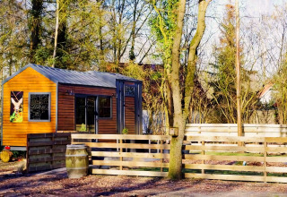Charming Tiny House met houten gevel en hek, omringd door bomen in een rustige omgeving in Nederland.