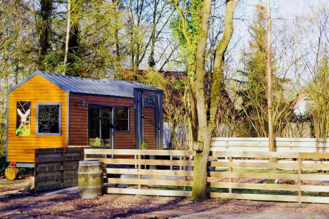Charming Tiny House de madera con cerca, rodeada de árboles en un entorno tranquilo en los Países Bajos.