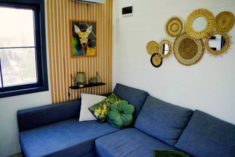 Woonruimte in Charming Tiny House in Nederland met blauwe bank, groene kussens en ronde wandspiegels.