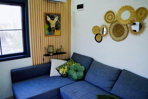 Sala de Charming Tiny House en Países Bajos con sofá azul, cojines verdes y espejos decorativos en la pared.