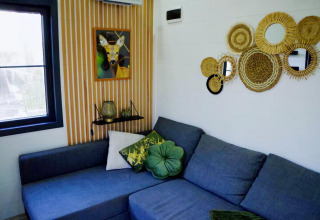 Sala de Charming Tiny House en Países Bajos con sofá azul, cojines verdes y espejos decorativos en la pared.